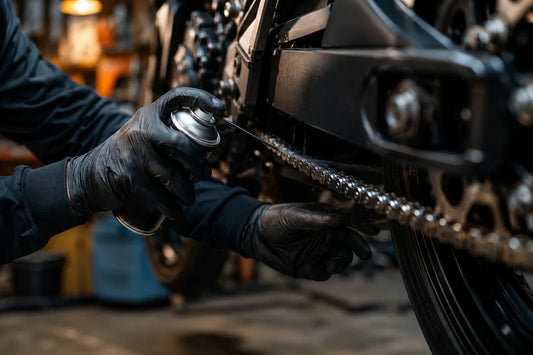 Mains gantées appliquant de la graisse sur une chaîne moto en atelier — guide entretien moto