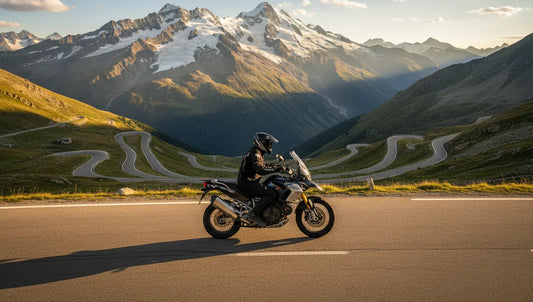 Motard sur route alpine sinueuse dans les Grandes Alpes françaises, panorama montagneux au golden hour